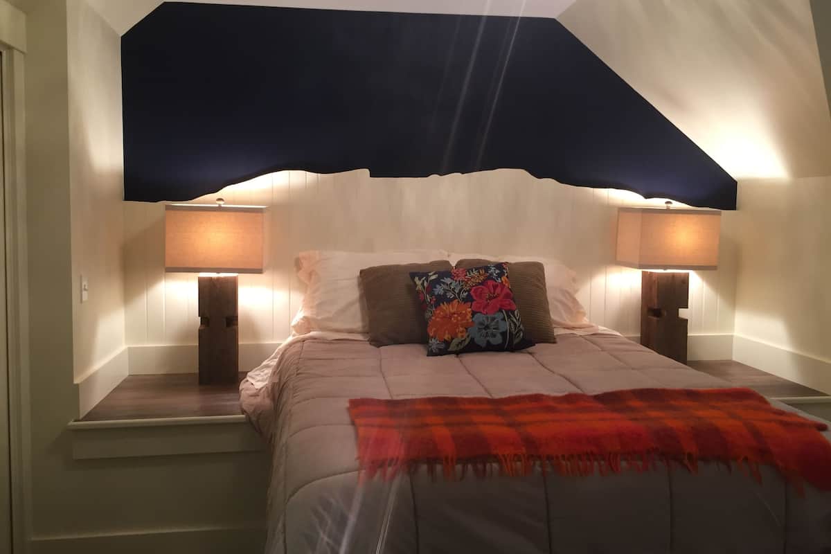 A bedroom with a bed, two bedside lamps, a nightstand, and a decorative pillow.