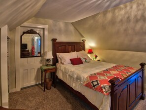 Un dormitorio con una cama de madera, una mesita de noche con lámpara, un espejo y una puerta.