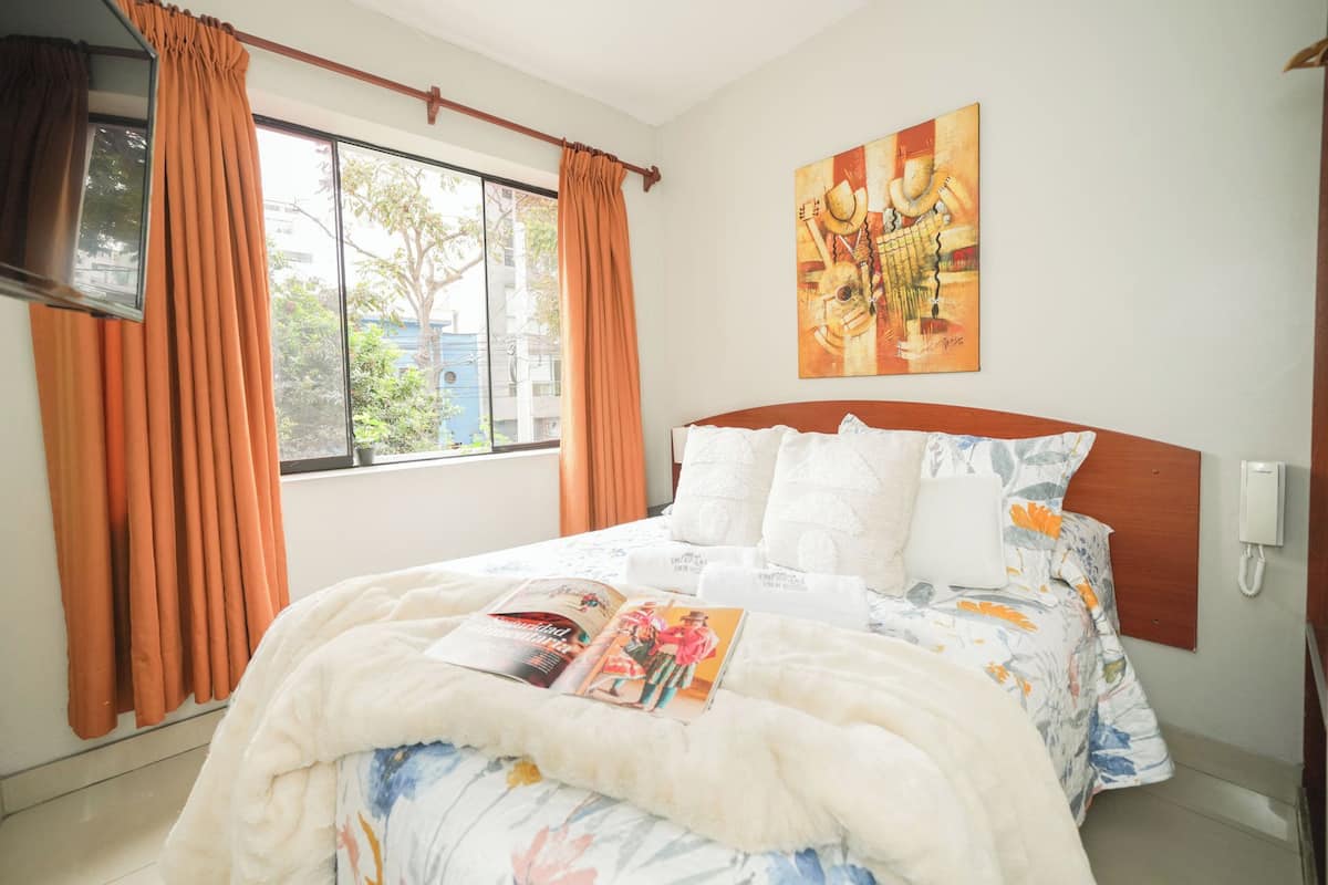 Cama bem arrumada com edredom floral, almofadas brancas e uma revista sobre a cama.