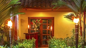 A stone pathway leading to a wooden door with a glass panel, surrounded by lush green foliage and illuminated by wall-mounted lights. - Hotel Boutique Iguana Verde (Orotina)