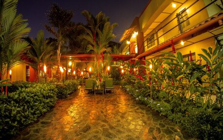 A courtyard with stone flooring, palm trees, and a building with a balcony.