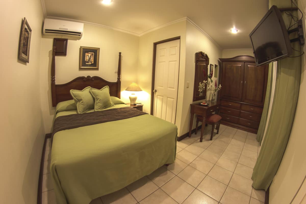 A hotel room with a bed, a desk, a wardrobe, and a television.