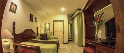 A hotel room with a wooden bed, a desk with drawers, a chair, a lamp, and a mirror.