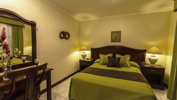 A neatly arranged hotel room with a large bed, two bedside tables with lamps, a wooden chair, a mirror, and a small table with a vase of flowers.