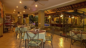 An indoor dining area with tables and chairs, ceiling fans, and a view of the outdoor patio. - Hotel Boutique Iguana Verde (Orotina)