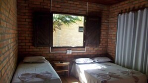 A small, cozy room with two single beds, a window with shutters, a small table, and a curtain. - Pousada do Riacho (Barreirinhas)
