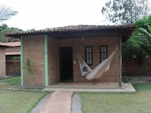 A small brick building with a door and windows, a hammock hanging over the door, and a paved pathway leading to the entrance.