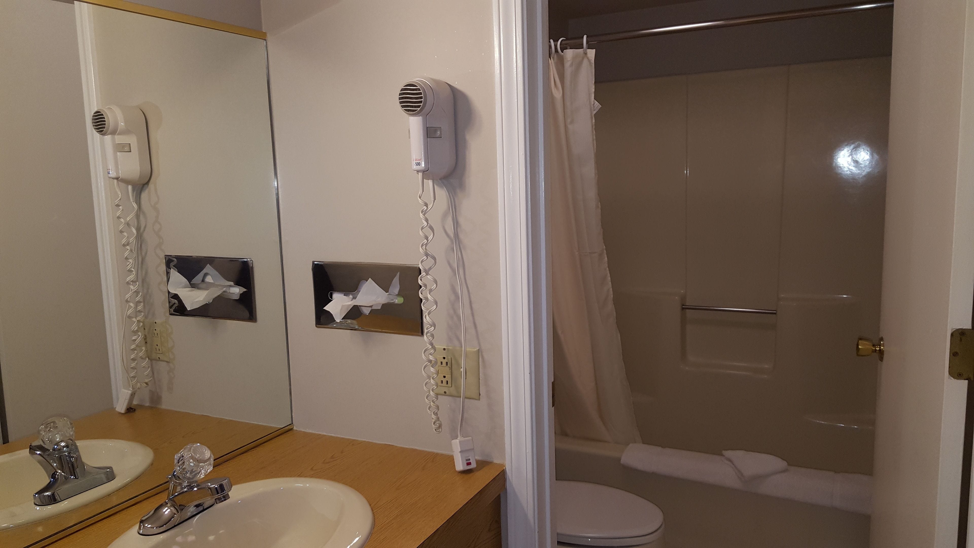 Een badkamer met wastafel, spiegel, haardroger en douchegordijn.