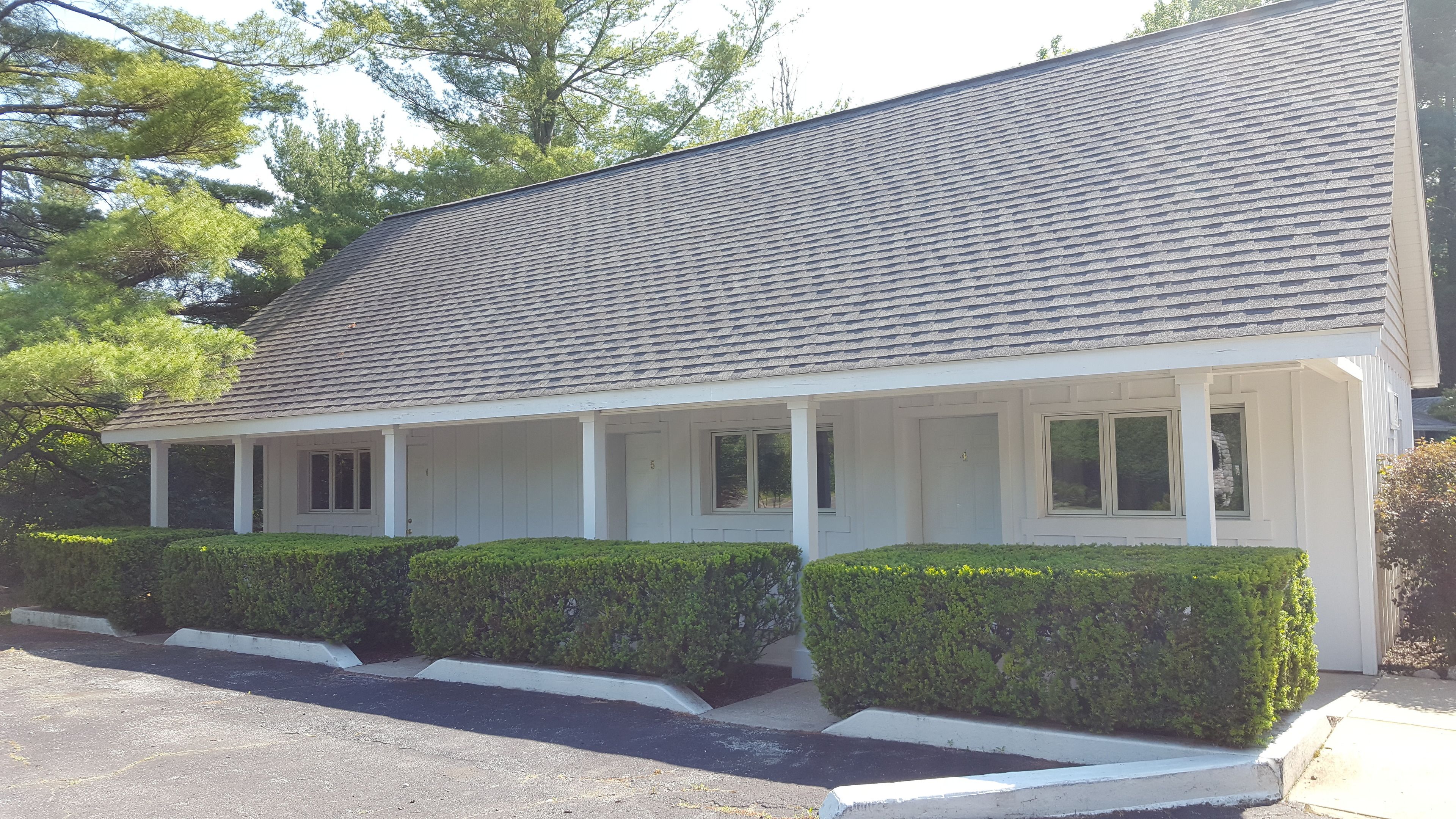 A single-story building with a gabled roof, a covered porch with multiple windows, and well-maintained hedges.