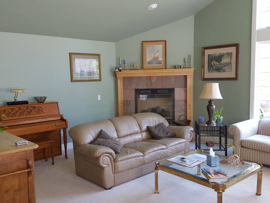 Una sala de estar con un sofá beige, una mesa de centro de cristal, un piano de madera y una chimenea.