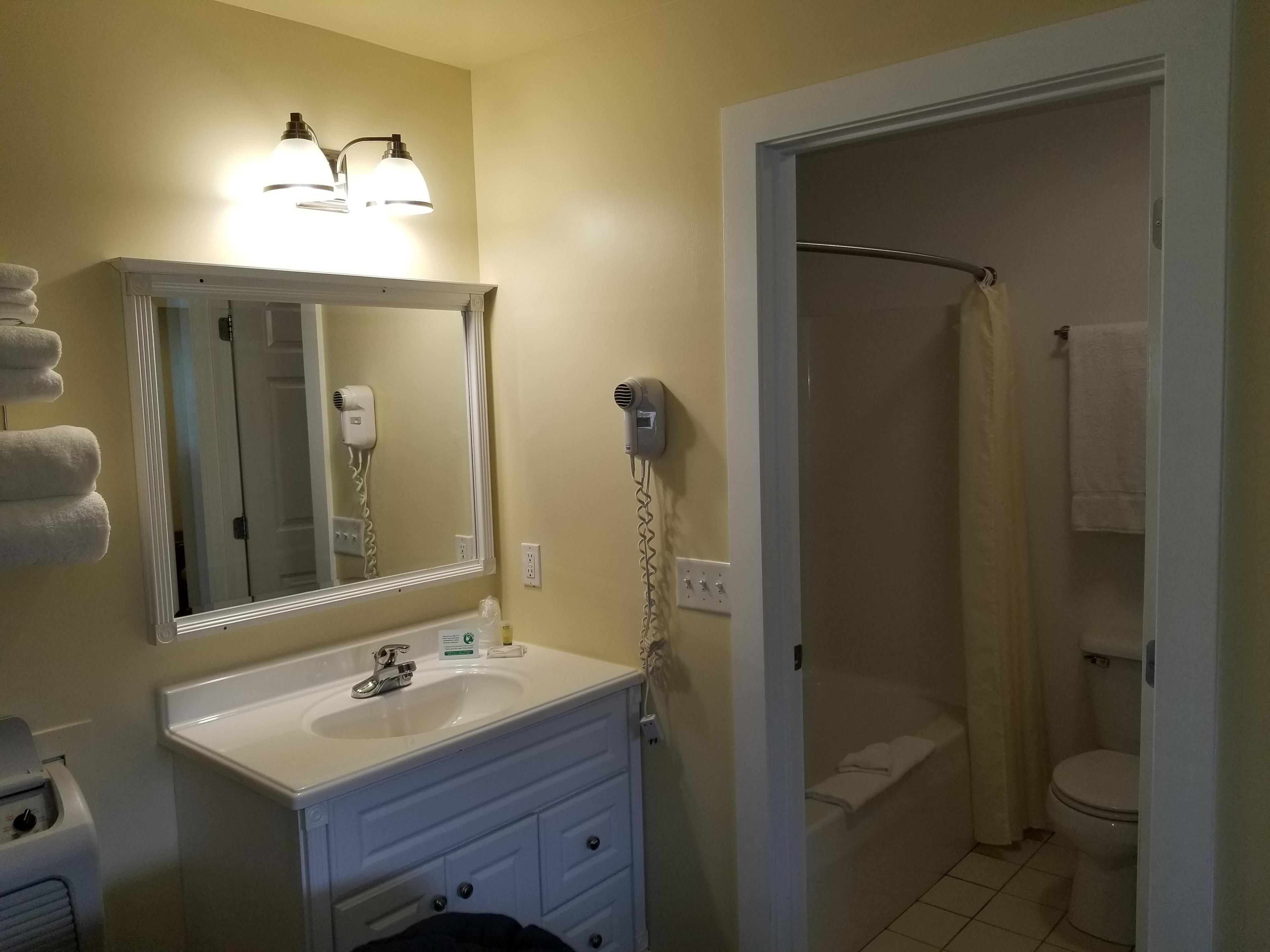 A bathroom with a sink, mirror, hair dryer, and shower.