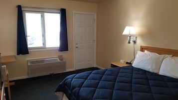 Habitación de hotel con cama, ventana con cortinas, puerta, mesita de noche con lámpara y radiador.
