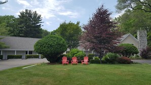 A motel with a parking lot, three red chairs in front of a tree, and a stone pillar. - Captain's Quarters Motel (Saugatuck)