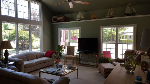 A spacious living room with large windows, a television, and a variety of seating options including a sofa and chairs. - Captain's Quarters Motel (Saugatuck)