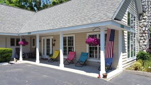 A building with a covered porch, a stone wall, and an American flag. - Captain's Quarters Motel (Saugatuck)