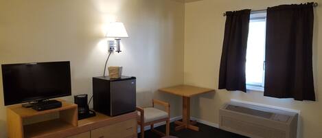 Habitación de hotel con televisión, escritorio, silla, cama, calefacción y ventana con cortinas.