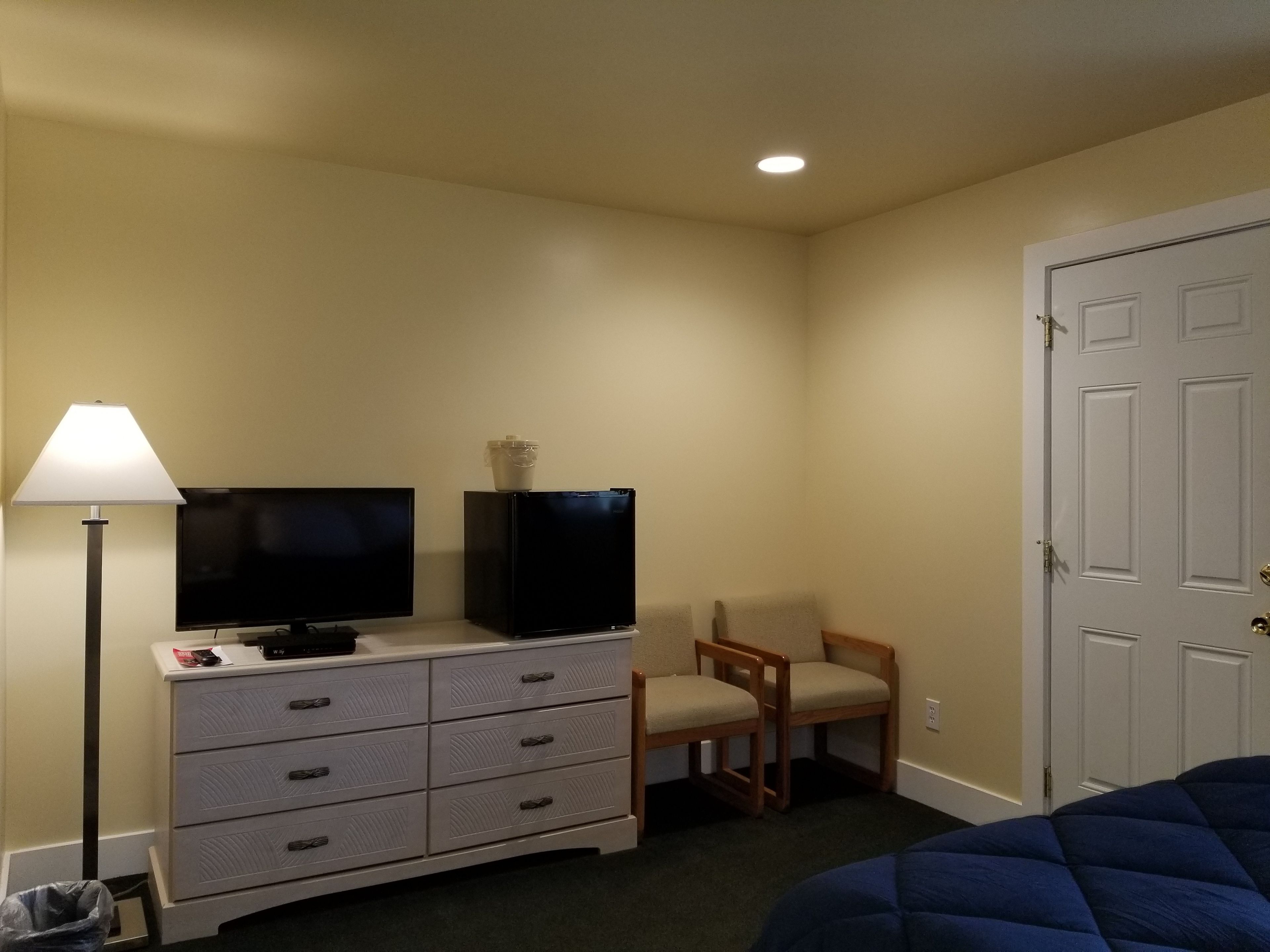 Habitación de hotel con televisión de pantalla plana sobre una cómoda, lámpara, dos sillas y una cama.