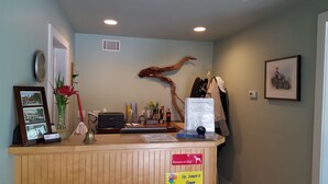 A reception desk with a 'Beware of Dog' sign, a framed picture of a building, a vase with flowers, and a menu board. - Captain's Quarters Motel (Saugatuck)