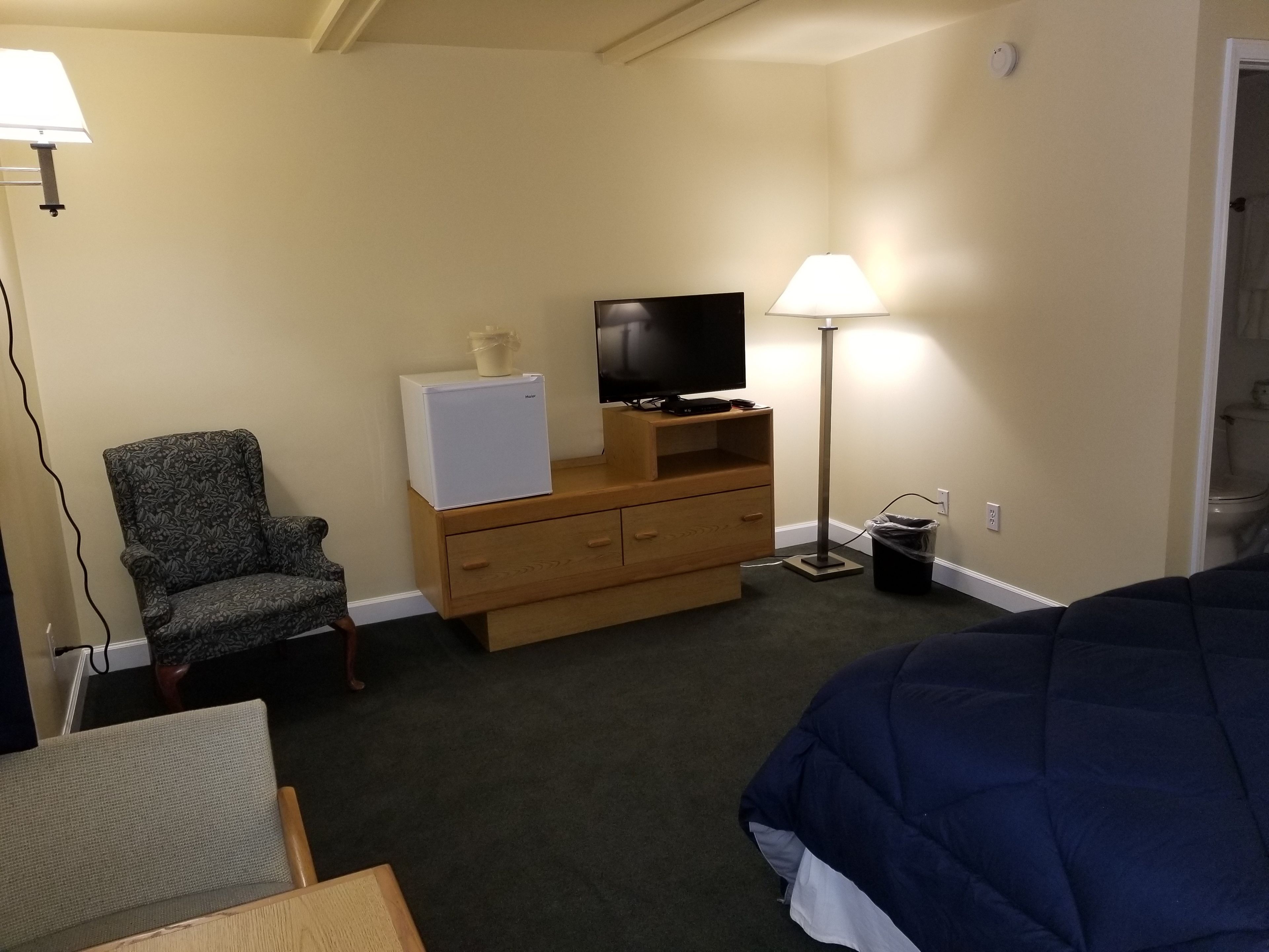 A hotel room with a bed, a chair, a dresser with a television, and a lamp.