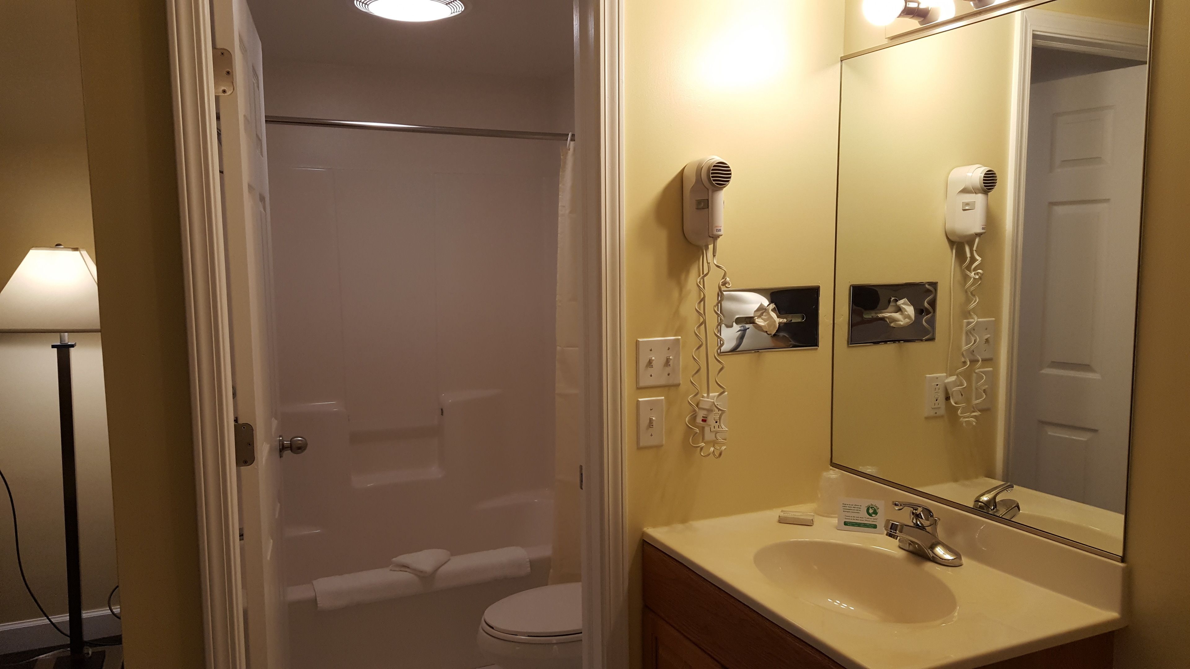 Un baño con inodoro, lavabo, espejo y secador de pelo fijado en la pared.