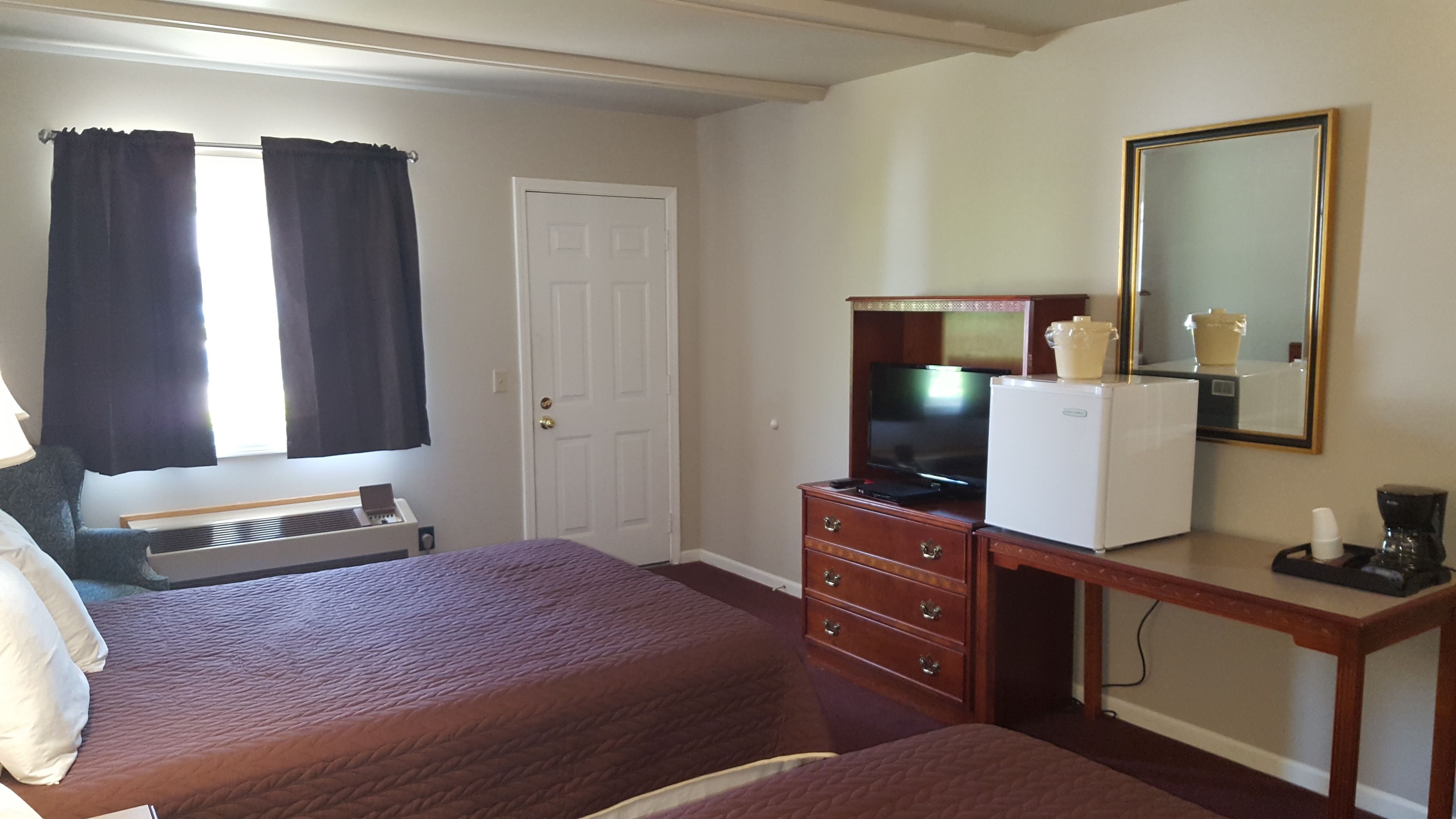 Ein Hotelzimmer mit einem Bett, einem Schminktisch mit Fernseher, einem kleinen Kühlschrank und einem Spiegel an der Wand.