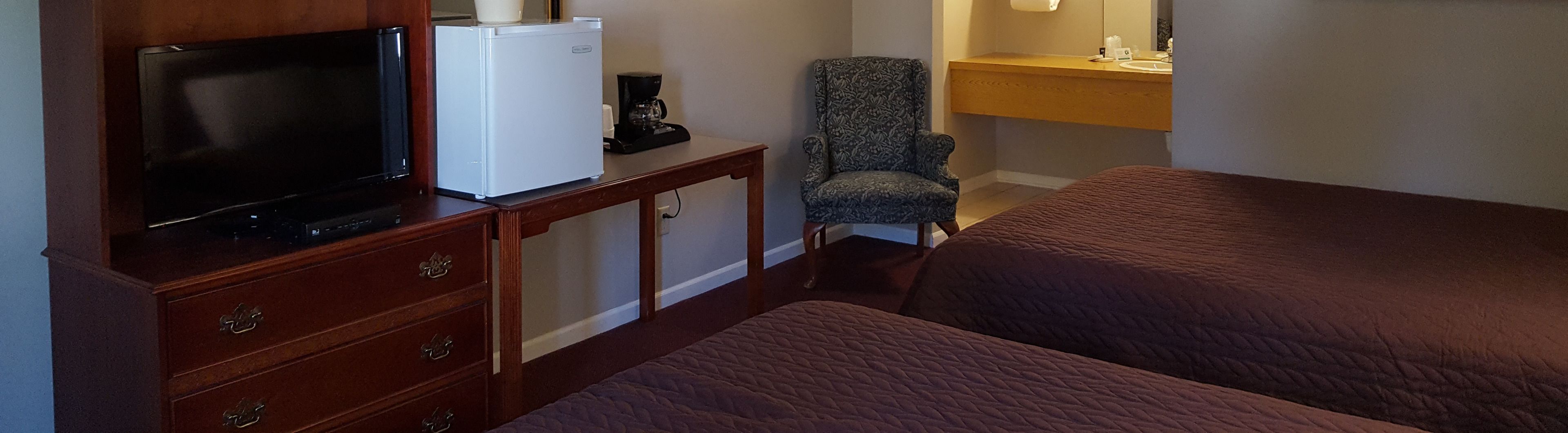 A hotel room with a TV, refrigerator, coffee maker, chair, and a bed.