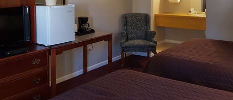 A hotel room with a TV, refrigerator, coffee maker, chair, and a bed.