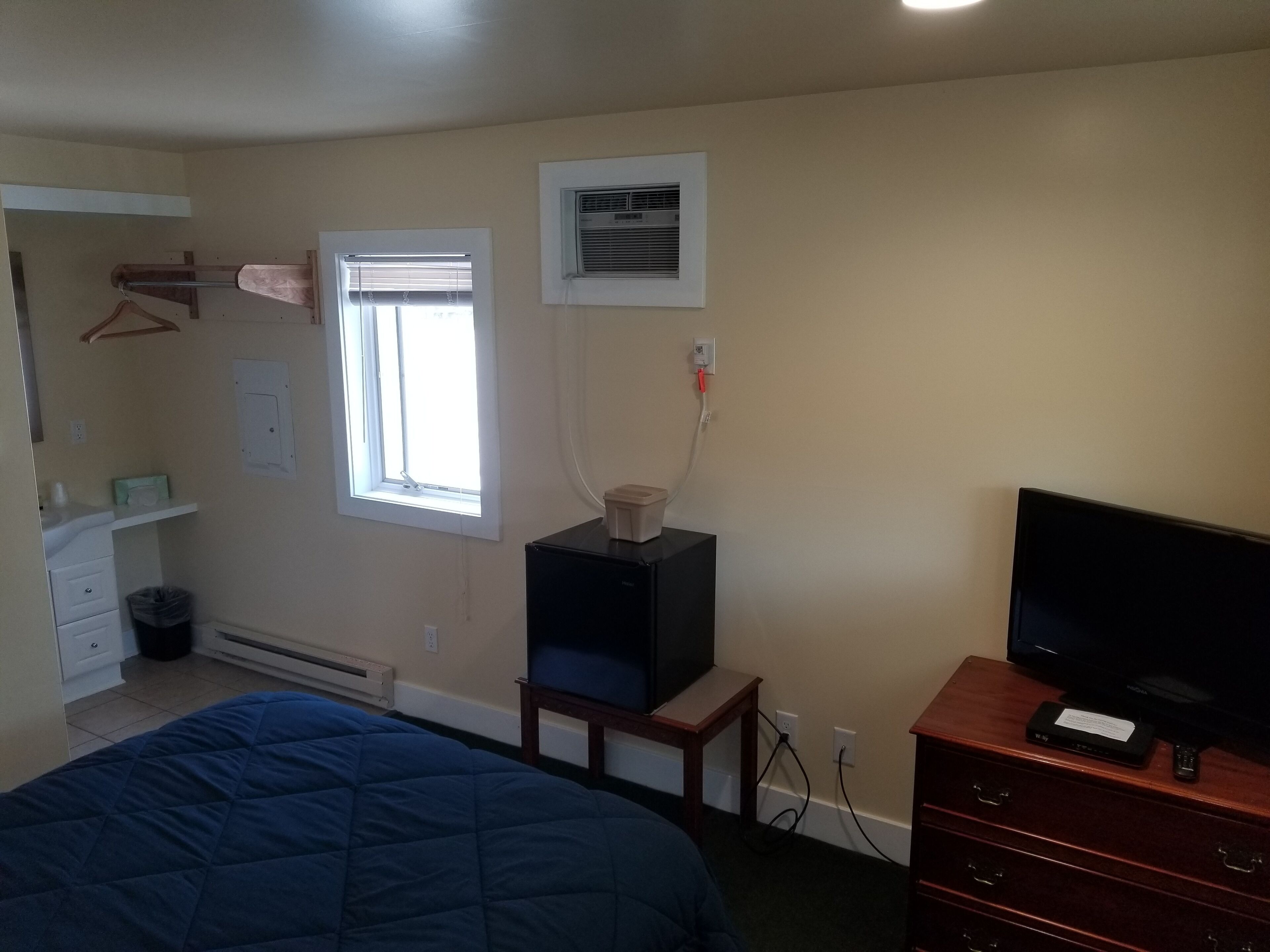 Une chambre à coucher comprenant un lit, une commode, un téléviseur et une fenêtre avec des stores.