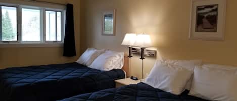 A hotel room with two beds, a nightstand, a lamp, and a framed picture on the wall.