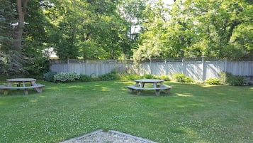 A backyard with two picnic tables, a wooden fence, and lush greenery.
