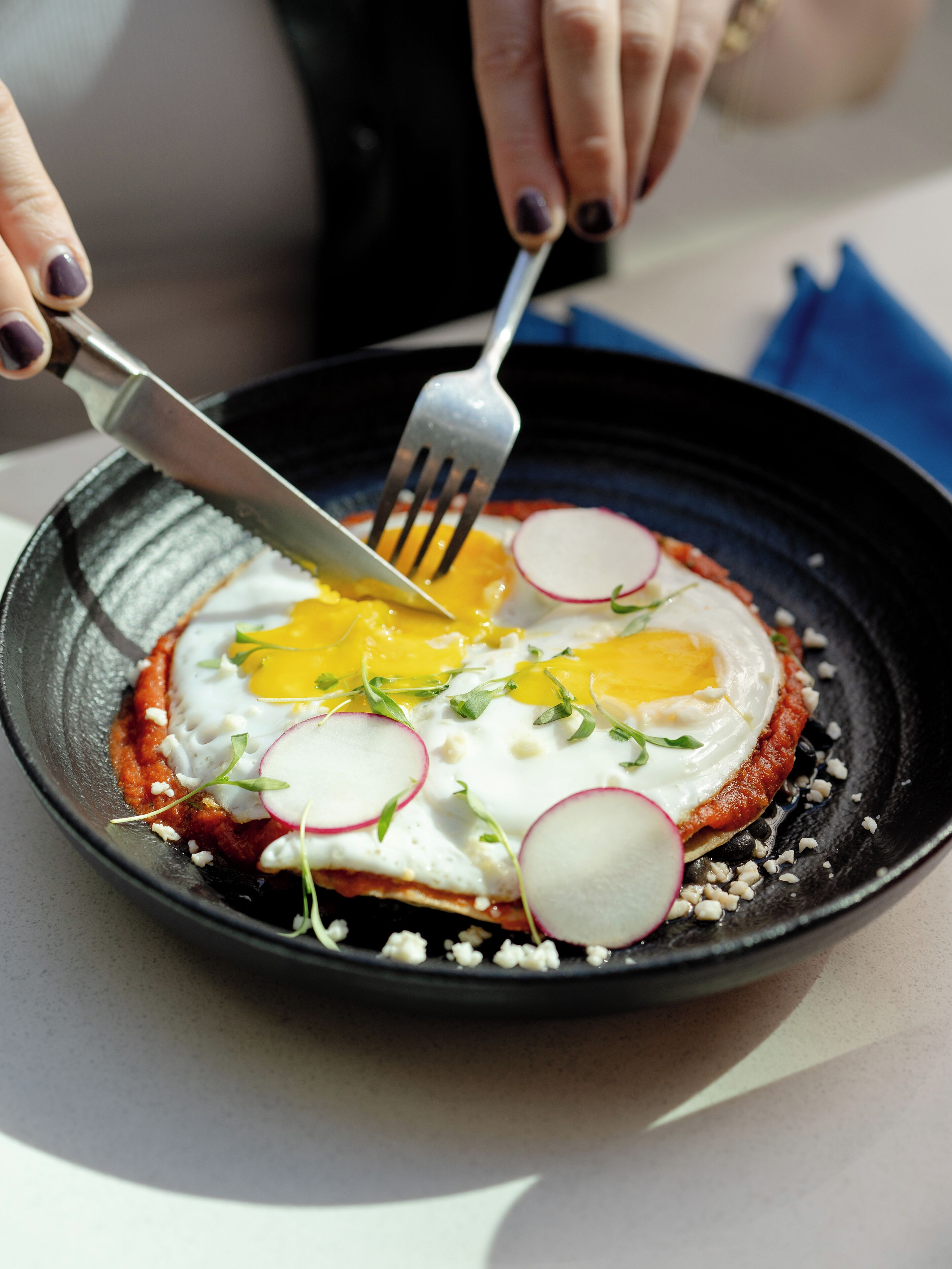 A close-up of a dish with an egg, radish slices, and greens on a black plate.