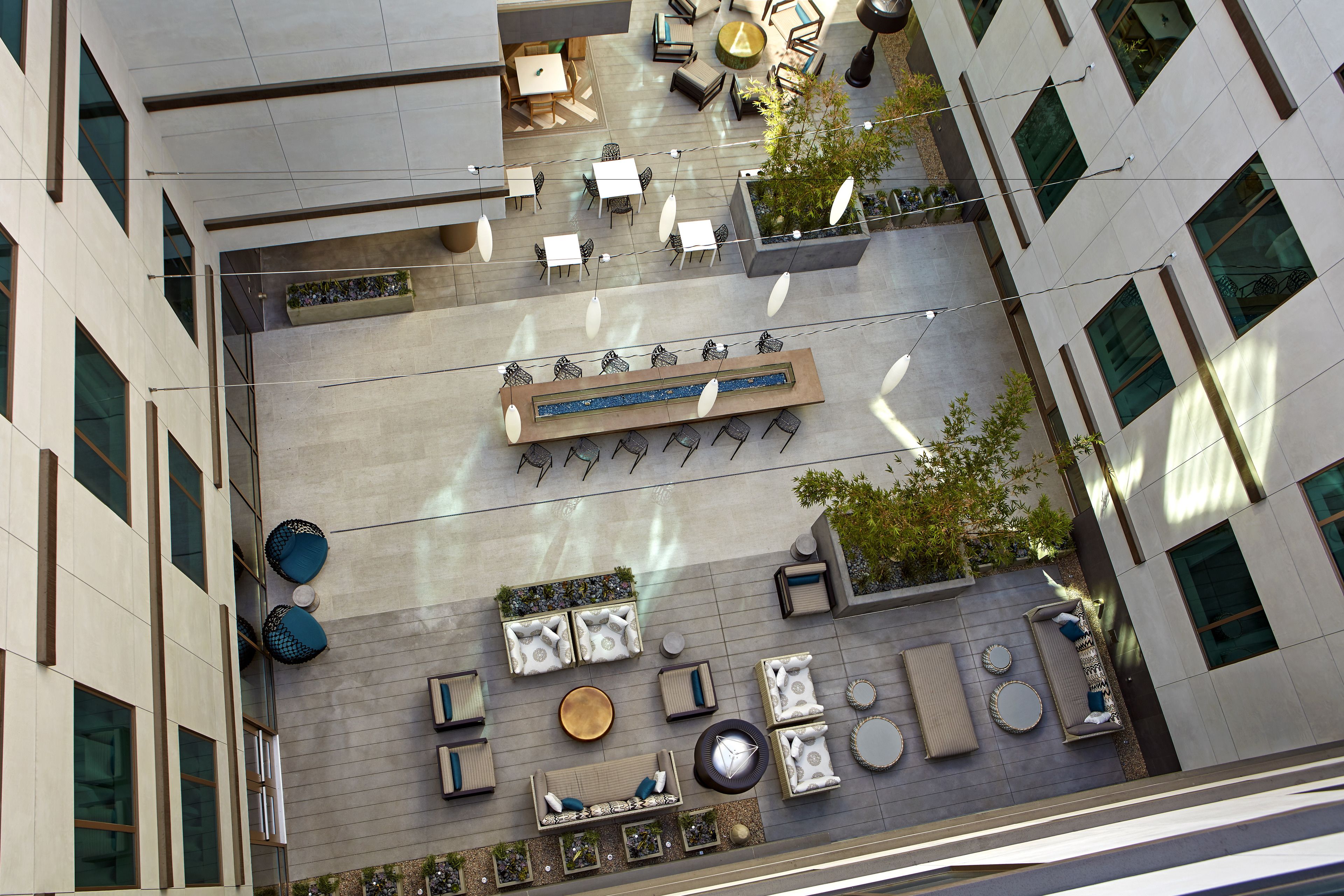 Une terrasse extérieure dotée de plusieurs espaces de détente, comprenant des canapés, des fauteuils et des tables, le tout entouré par la façade moderne d’un immeuble.