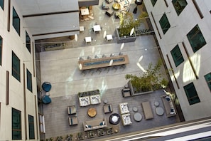 Una terraza al aire libre con varias zonas de estar, incluyendo sofás, sillas y mesas, rodeada por la fachada moderna de un edificio.