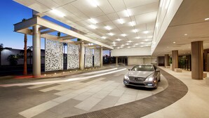 Ein moderner Hotelzugang mit einem darin abstellendem Auto, mit überdachtem Gang und dekorativen Verkleidungen.