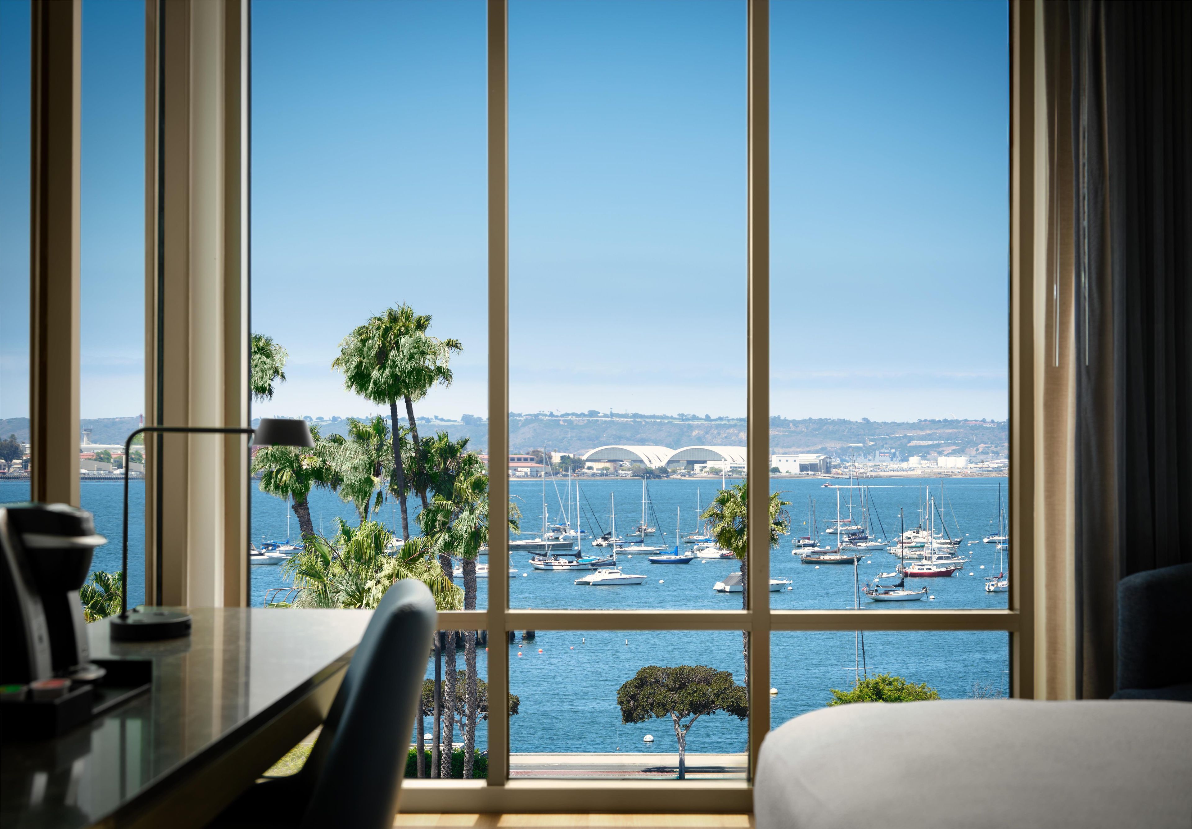A room with a large window overlooking a marina with boats and a bridge in the distance.