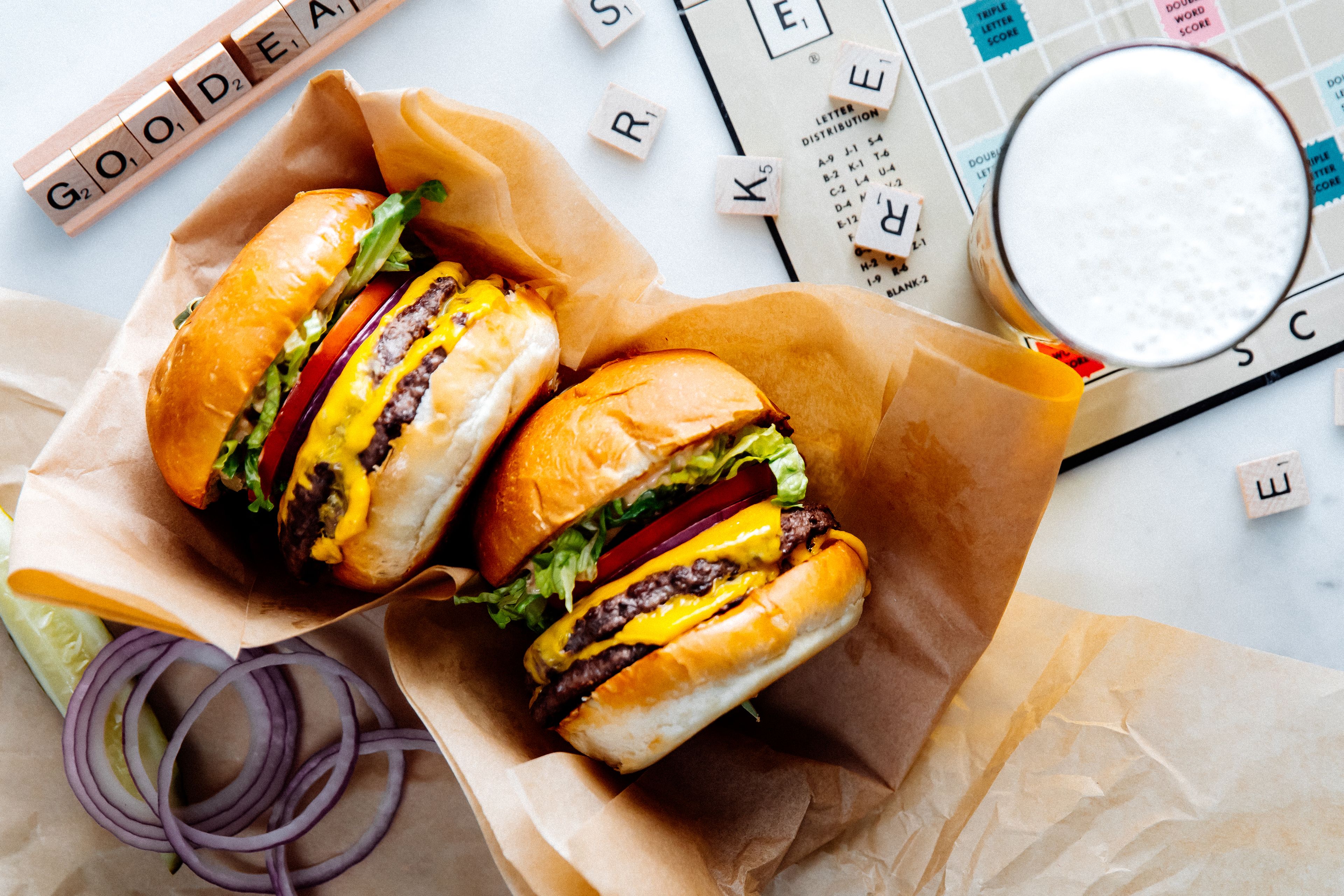Deux hamburgers sur une assiette en papier, un verre de lait et des lettres de Scrabble.