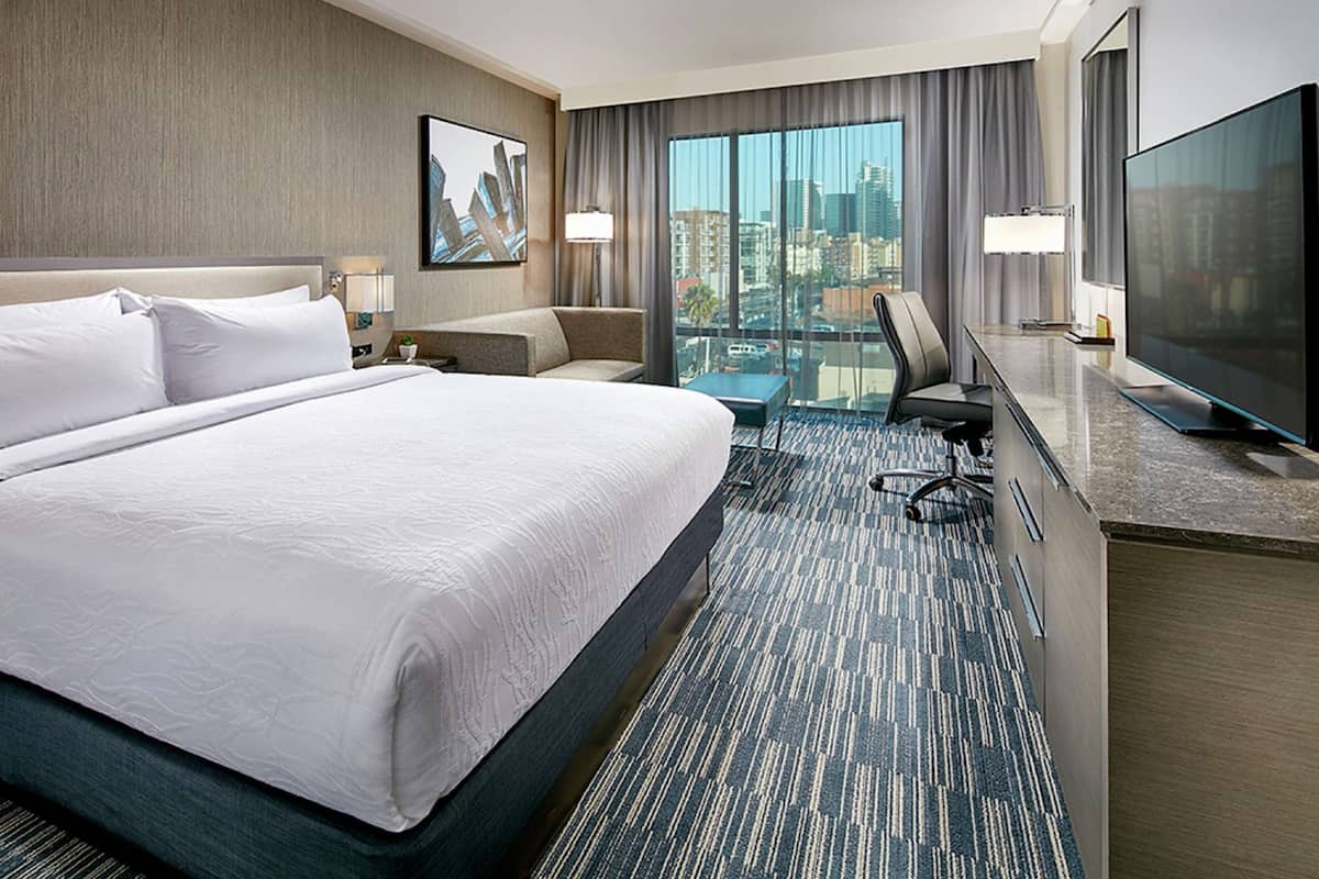 Habitación de hotel con una cama grande, un escritorio, un televisor y vistas a la ciudad.