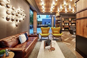 A modern interior with a leather sofa, yellow chairs, a coffee table, and a bookshelf. - Hilton Garden Inn San Diego Downtown/Bayside (San Diego)