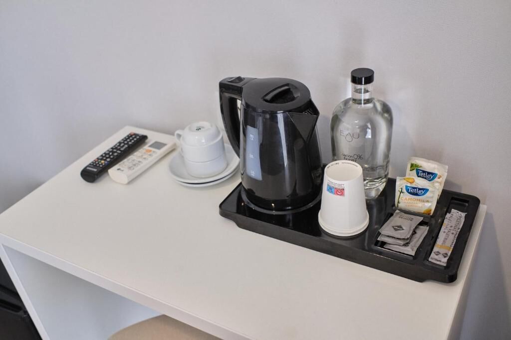 A hotel room's coffee station with a remote control, coffee maker, cup, sugar packets, and a bottle.