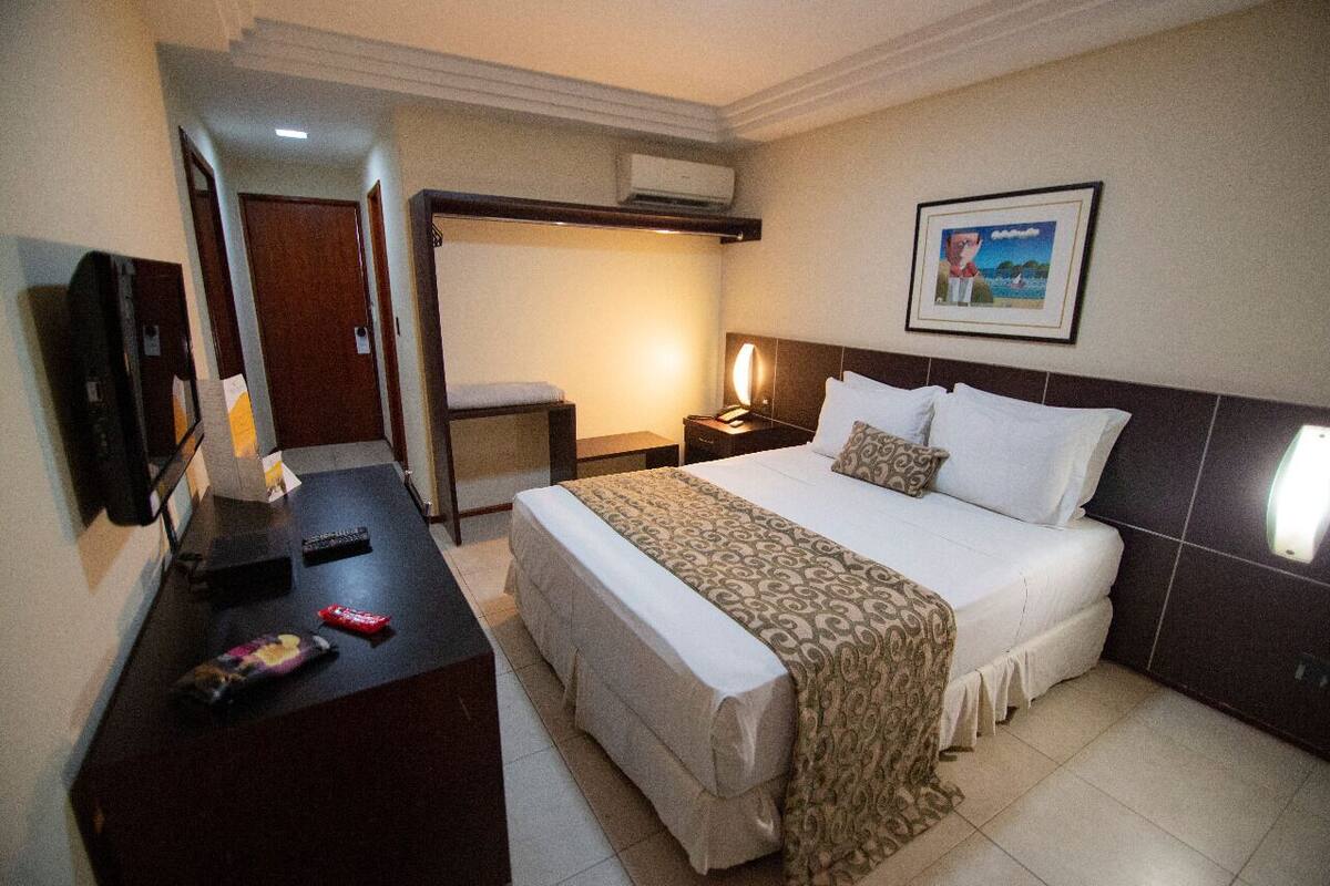 A hotel room with a bed, bedside table, lamp, and a framed picture on the wall.