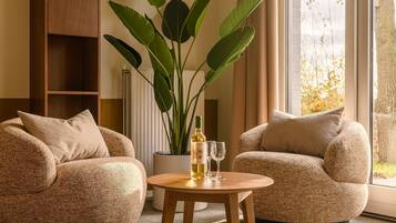 Two textured armchairs facing each other with a small round wooden table between them, a bottle of white wine, and two glasses on the table.
