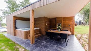 A modern outdoor hot tub area with a wooden deck, a table with chairs, and a stone-tiled floor.