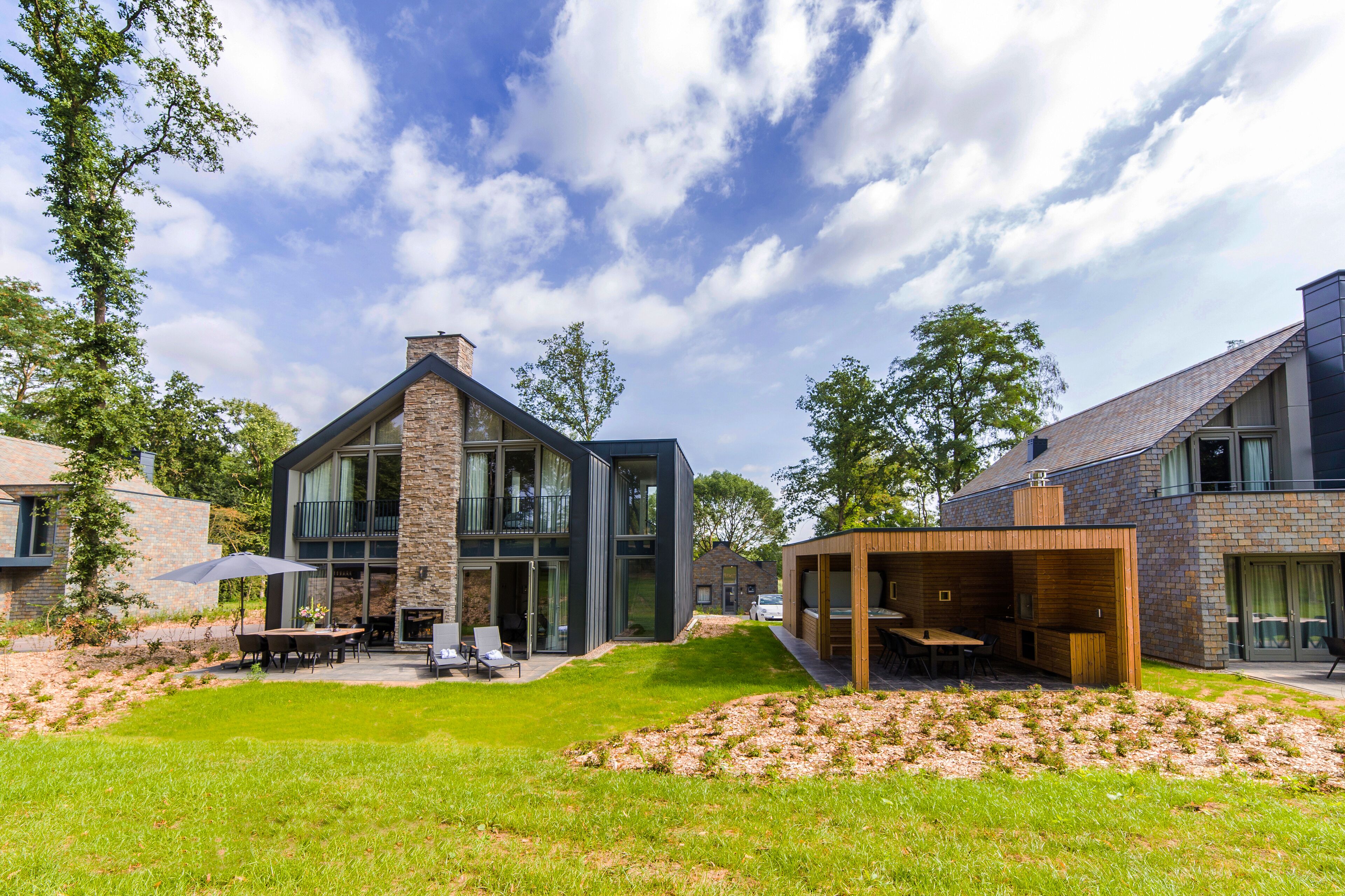 A modern house with a spacious backyard, a covered outdoor dining area, and a stone fireplace.