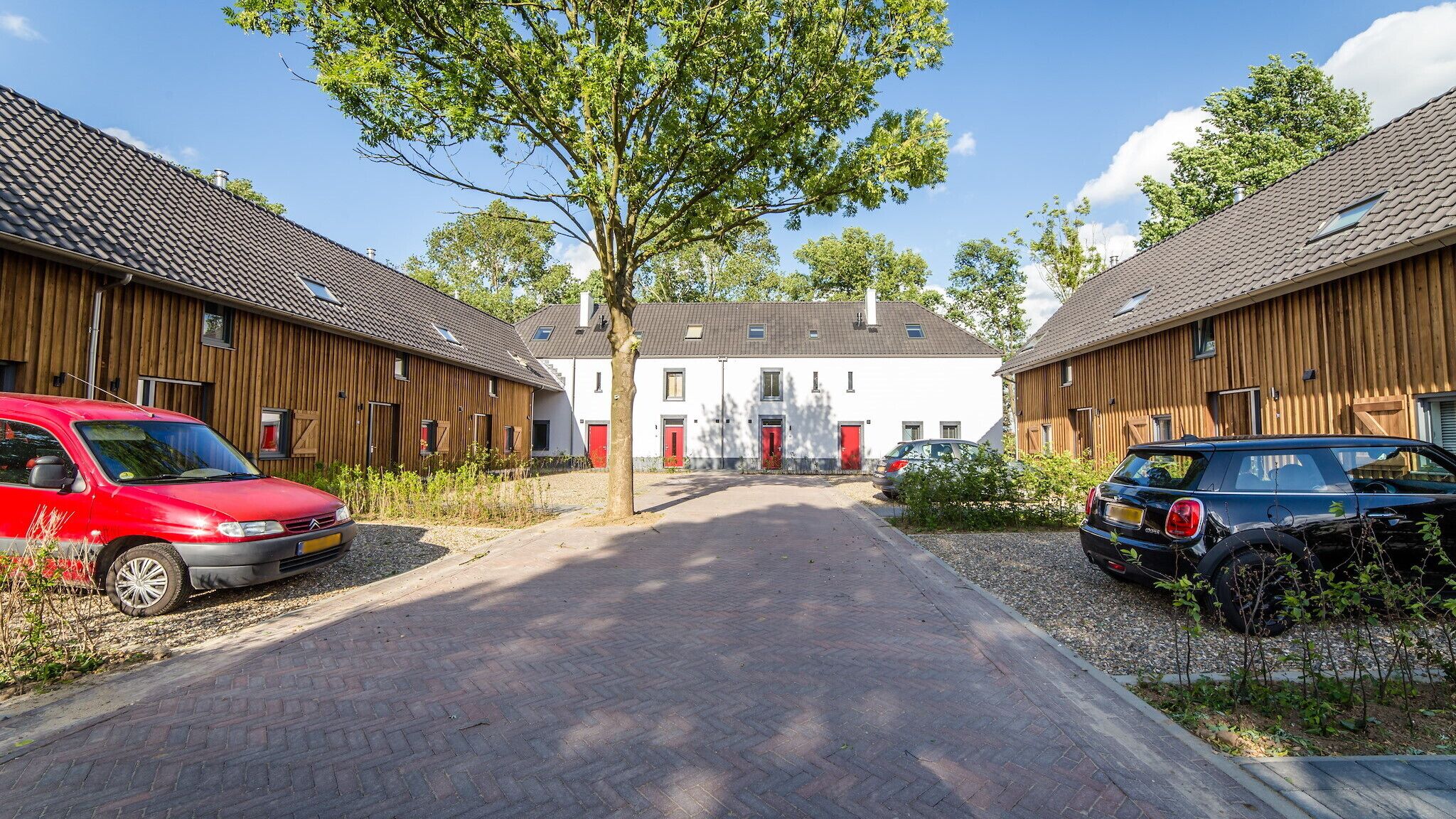 Een woonstraat met houten huizen, een centraal wit gebouw en geparkeerde auto's.