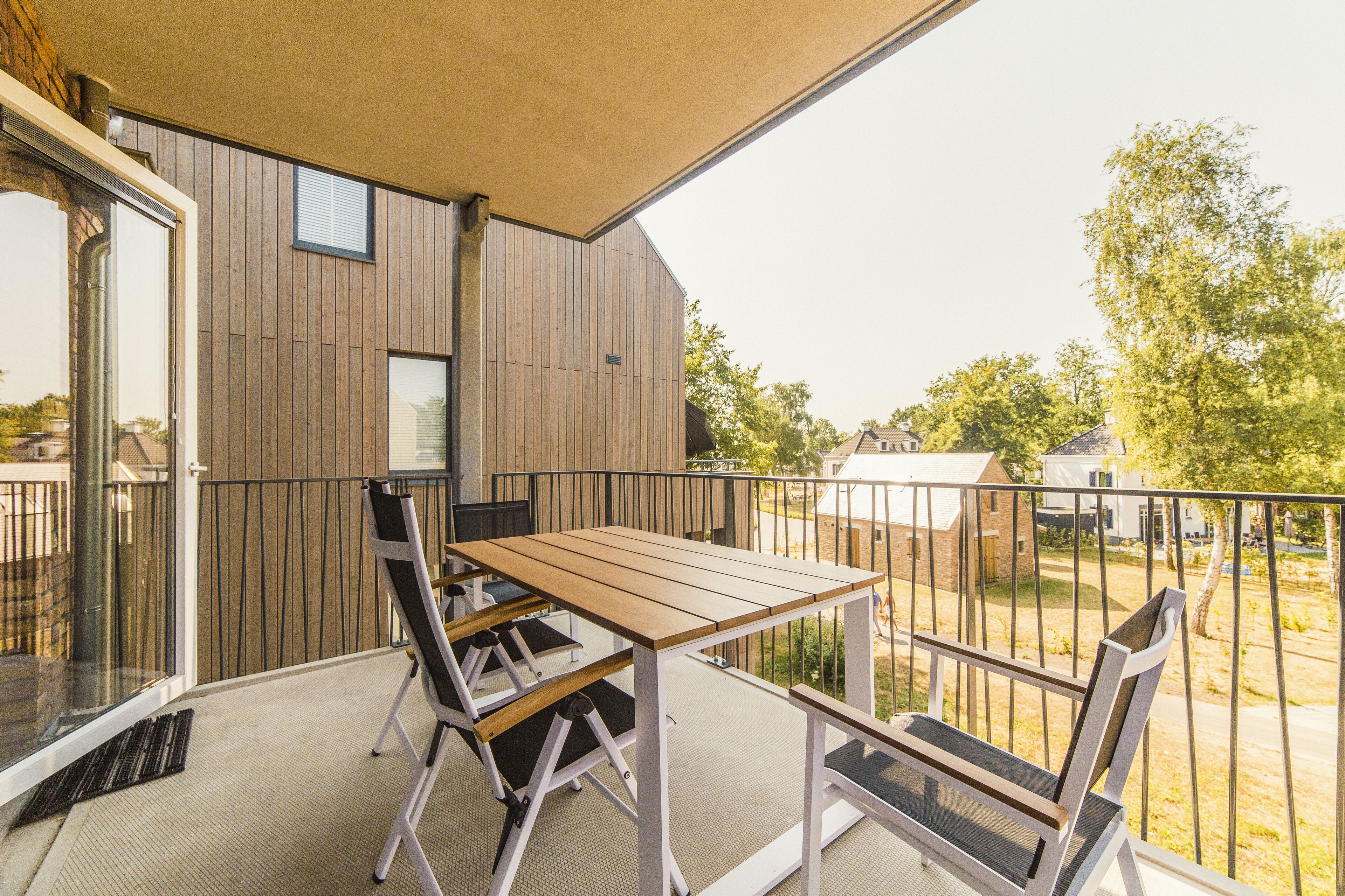 A balcony with a wooden table and chairs, a sliding glass door, and a view of the surrounding area.