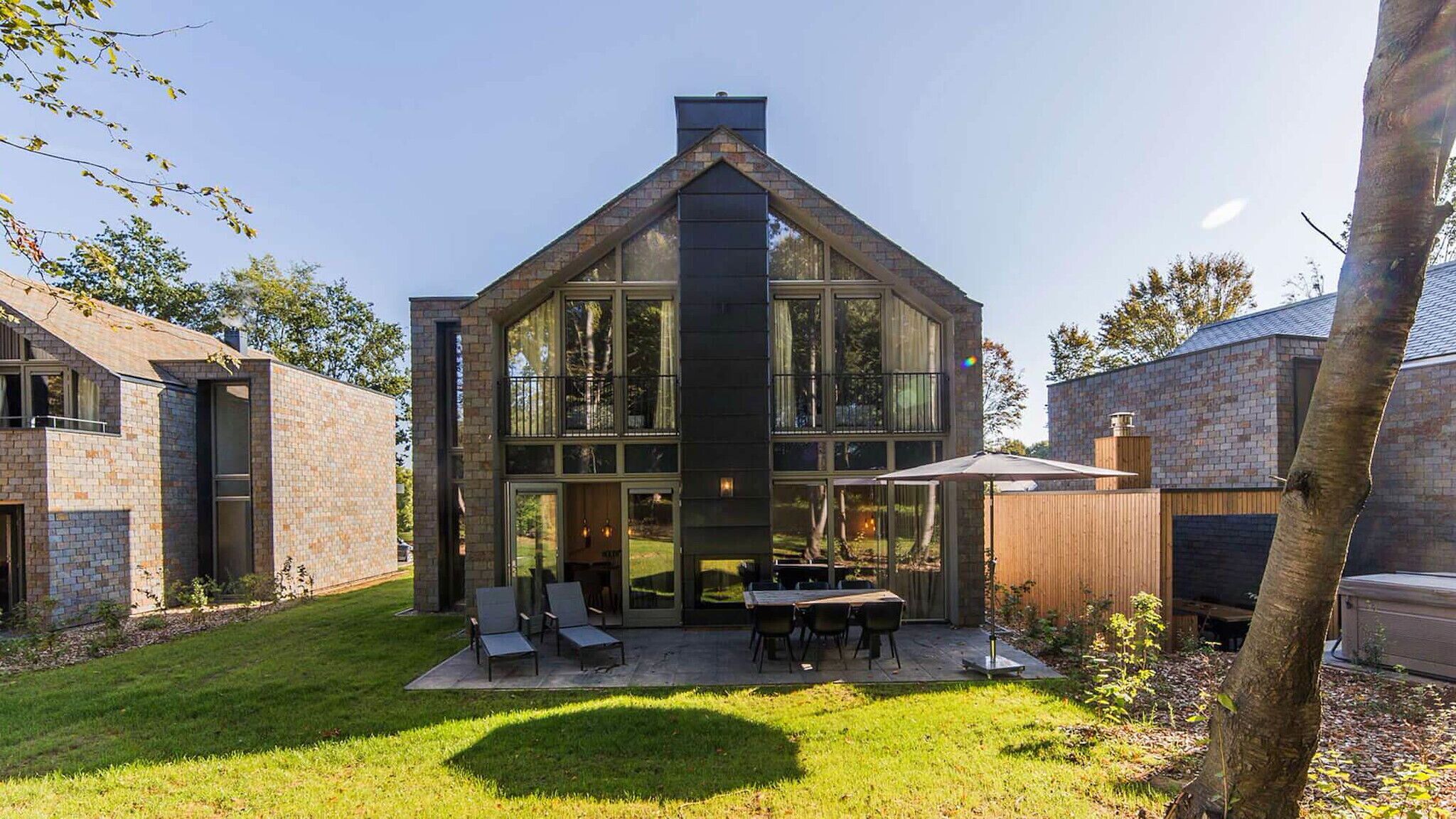 A modern house with a large glass front, a patio with outdoor furniture, and a brick exterior.