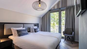 Une chambre d’hôtel moderne, dotée d’un grand lit, d’une table de chevet, d’une chaise et offrant une vue sur l’extérieur grâce à de grandes fenêtres.