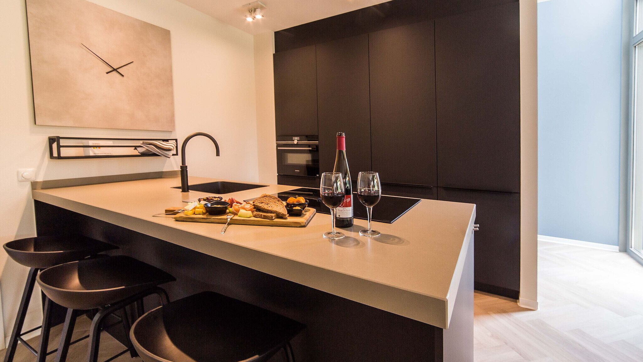 Una cocina moderna con una isla central, armarios oscuros y un amplio ventanal.