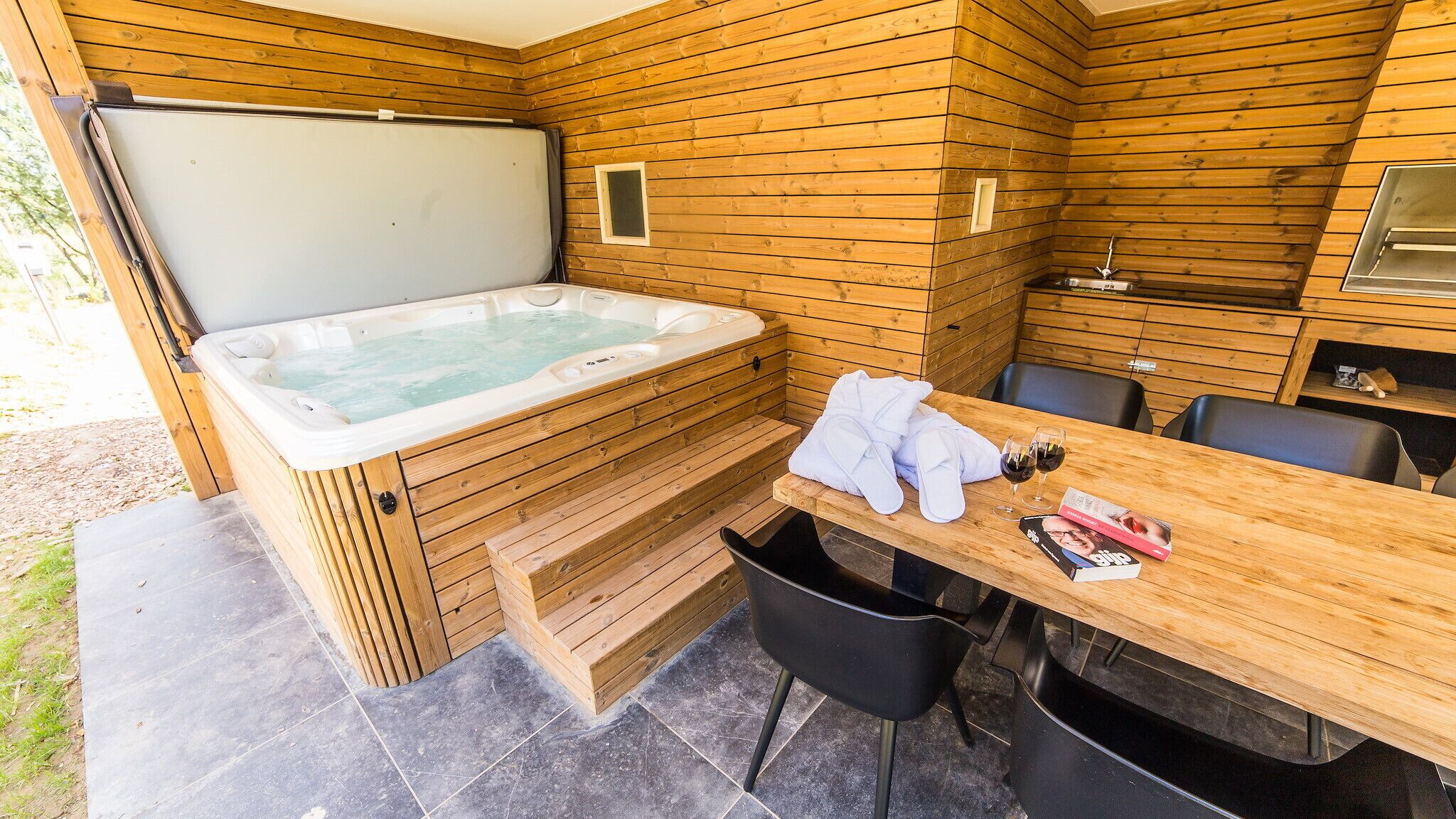 Une cabane en bois avec un bain à remous, une table avec des chaises et un petit coin cuisine.