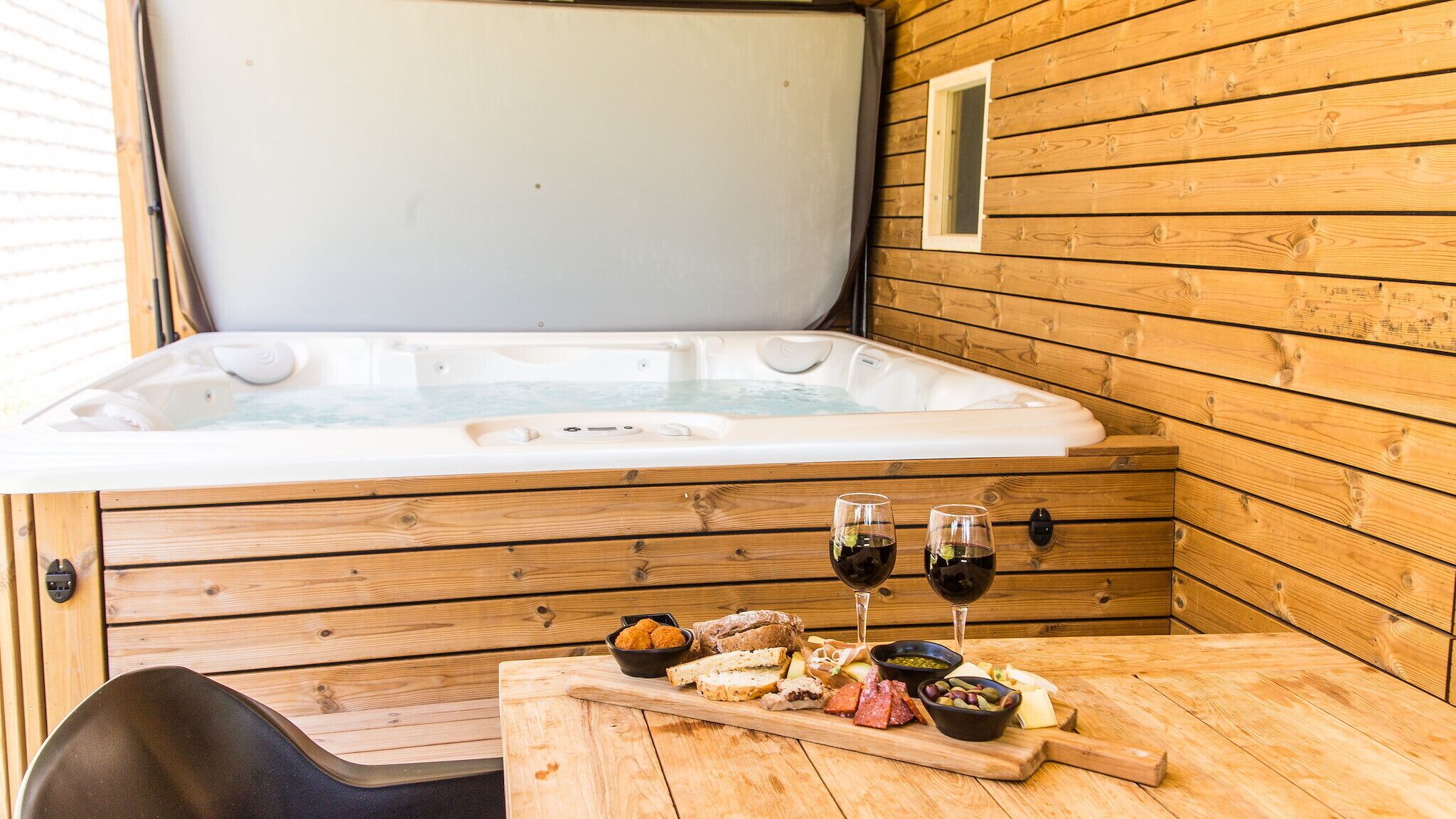 Eine Holzhütte mit Whirlpool, einem Tisch mit Snacks und Weingläsern sowie einer Bank.